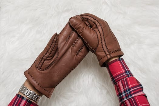 closeup men's hand taking off the brown leather gloves over white fur.