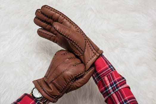 closeup men's hand wearing the brown leather gloves over white fur.