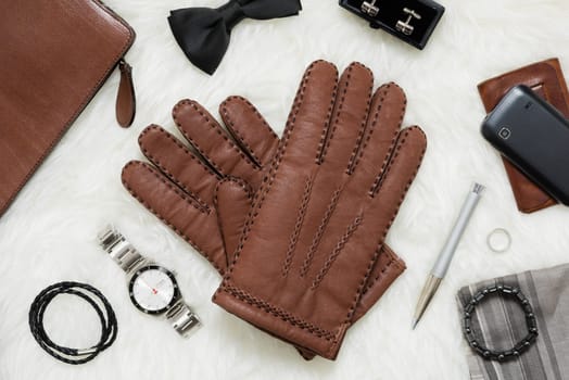 Pair of men's brown leather gloves and other men's accessories over white fur.