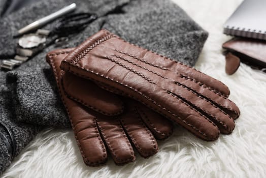 Pair of men's brown leather gloves and other men's accessories over white fur.