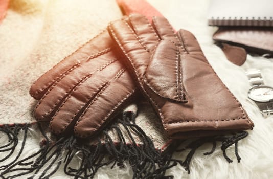 Pair of men's brown leather gloves and other men's accessories over white fur.