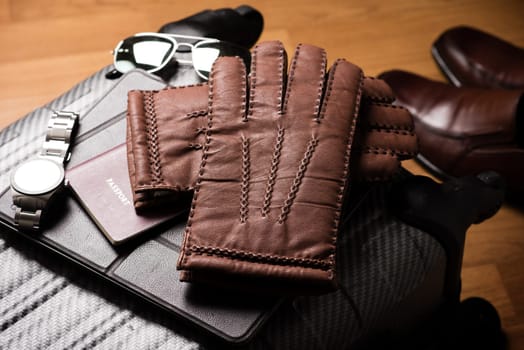 Pair of men's brown leather gloves and other men's accessories on the luggage.