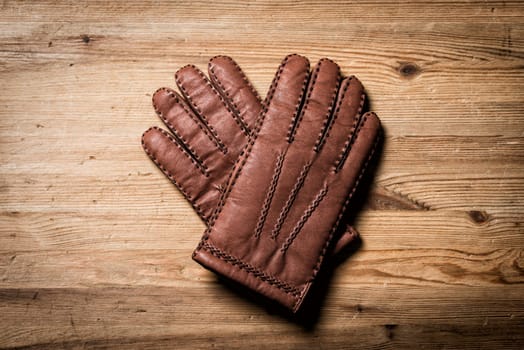 Pair of men's brown leather gloves isolated over wood background.