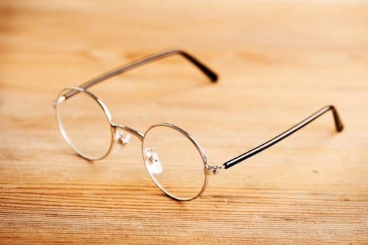 closeup round frame style of eyeglasses on wooden desk, shallow depth of field