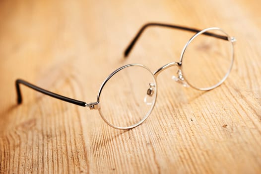 closeup round frame style of eyeglasses on wooden desk, shallow depth of field