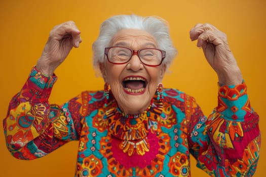 A happy and playful elderly woman in colored clothes on a yellow background.