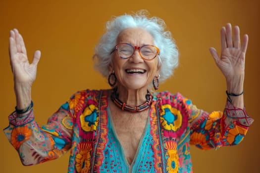 A happy and playful elderly woman in colored clothes on a yellow background.