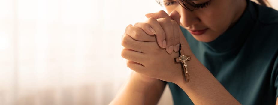 Young beautiful believer prays for happiness while holding crucifix.Concept of hope, religion, faith, christianity, spiritual, trust and god blessing.Bright white blurring background. Burgeoning.