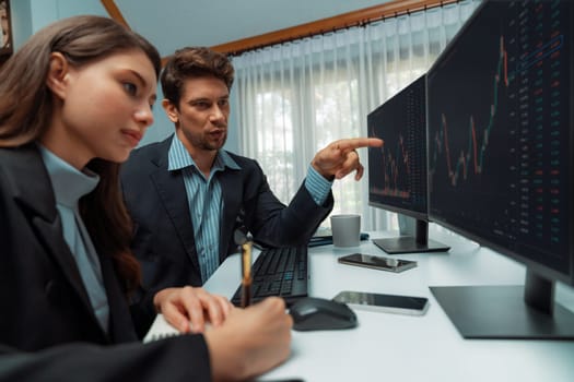 Two business traders consulting dynamic stock market in currency rate investment trading on two computer screens, woman coworker taking note with compare real time graph at modern office. Postulate.