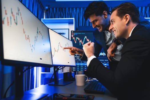 Cheerful two stock exchange traders raising fist up for digital currency achievement focusing on dynamic data background. Successful investors earning high profit analyzed by market graph. Sellable.