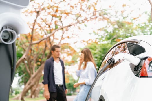 Lovely young couple recharging battery for electric car during autumnal road trip travel EV car in autumnal forest. Eco friendly travel on vacation during autumn. Exalt