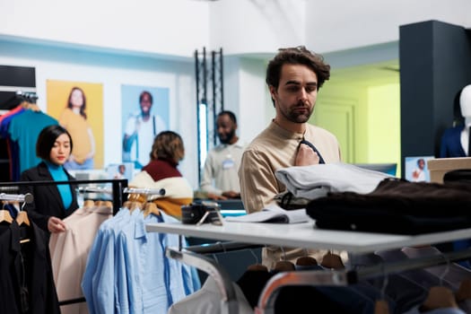 Clothing store client selecting menswear and accessory while choosing wardrobe outfit. Young caucasian man searching for tie and shirt while shopping in department mall boutique