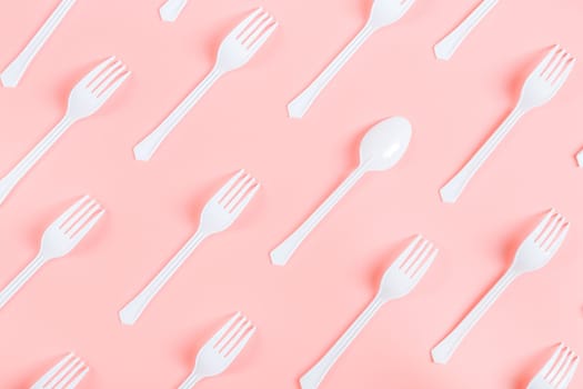 White plastic forks with one spoon lie diagonally on a pink background, flat lay close-up. Ecology concept, template, banner.