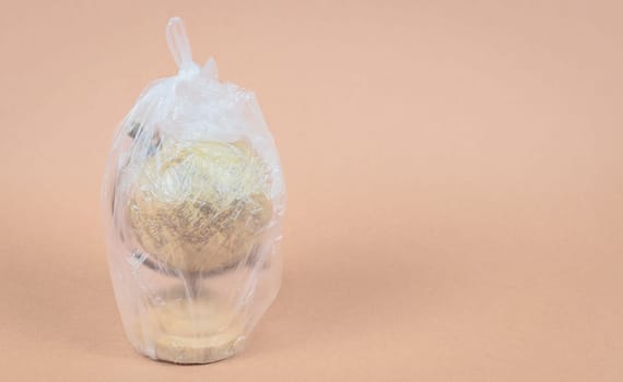 One planet earth globe inside a plastic bag stands on the left on a beige background with copy space on the right, side view close-up.