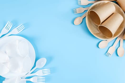 One row of plastic and one row of paper disposable tableware with cutlery lie on the sides on a pastel blue background with copy space in the center, close-up, flat lay closeup. The concept is environmentally friendly, waste sorting and recycling.