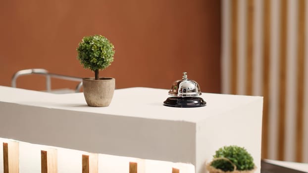 Elegant concierge bell on modern stylish hotel lobby check in desk. Reception bell next to mini plant on empty warm hospitality industry lounge reception counter, close up