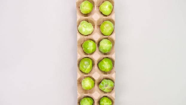 Raw organic Brussel sprouts in brown egg container on grey background, top view. Flat lay, overhead, from above. Copy space