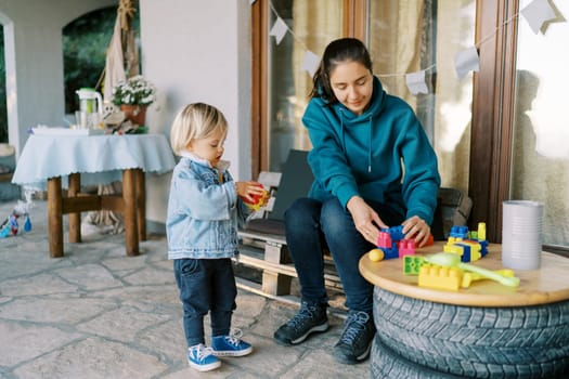 Mom with a little girl assembles a Lego constructor on a table sitting on a bench near the house. High quality photo