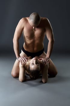 Nude paired yoga. Middle aged man rests on shoulders of young woman