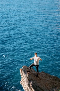 Young smiling man standing on a stone ledge above the sea with his thumbs up. High quality photo