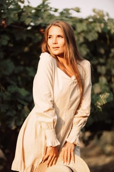 Woman stands in front of vineyard. She is wearing a light dress and posing for a photo. Travel concept to different countries.