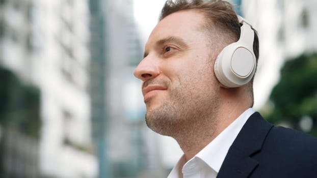 Close up of businessman listen headphone and dancing to relaxing music with cheerful and motivation. Skilled project manager enjoy to listen relaxed song with blurred background at urban city. Urbane.