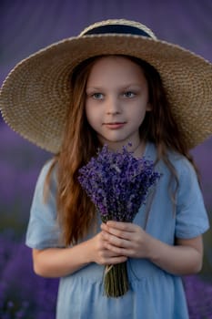 Girl lavender field in a blue dress with flowing hair in a hat stands in a lilac lavender field.
