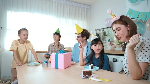 Caucasian mother cutting cake while family congratulate in girl's birthday. Diverse family celebrate daughter important day while waiting for eating dessert and food while smiling together. Pedagogy.