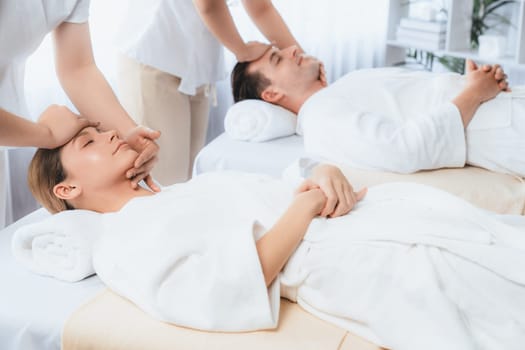 Caucasian couple enjoying relaxing anti-stress head massage and pampering facial beauty skin recreation leisure in dayspa modern light ambient at luxury resort or hotel spa salon. Quiescent