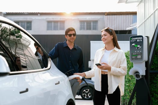 Eco-friendly conscious family couple recharging EV vehicle from home charging station. EV electric car technology utilized as alternative transportation for future sustainability. Expedient