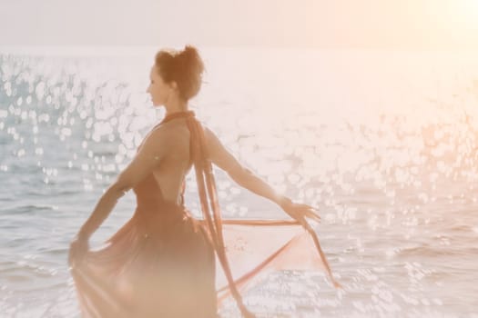 Side view a Young beautiful sensual woman in a red long dress posing on a rock high above the sea during sunrise. Girl on the nature on blue sky background. Fashion photo.