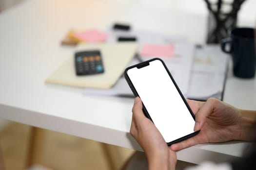 Unrecognizable businesswoman hands holding mobile phone with white screen sitting at desk.