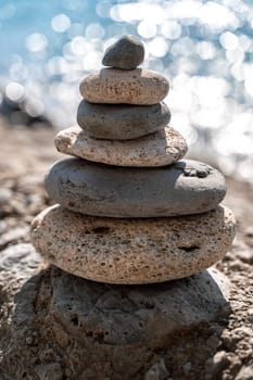 A tower of stones. Balanced pyramid of pebbles on the beach on a sunny day. Blue sea in the background. Selective focus, bokeh. Zen stones on the sea beach, meditation, spa, harmony, tranquility, balance concept. Vertical photo