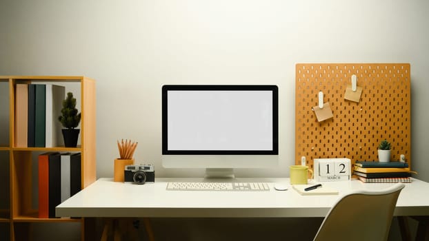Creative workplace with blank computer monitor, camera, coffee cup and peg board on wall.