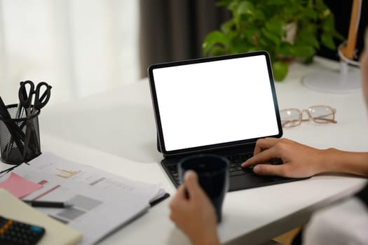 Closeup young businesswoman holding coffee cup and typing on keyboard of digital tablet.