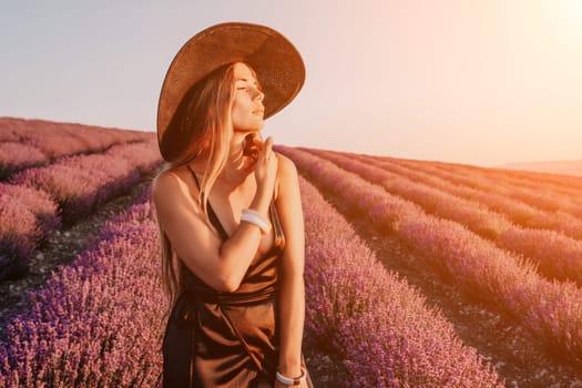 Close up portrait of young beautiful woman in a white dress and a hat is walking in the lavender field and smelling lavender bouquet.