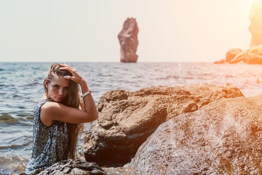 Woman travel sea. Young Happy woman in a long red dress posing on a beach near the sea on background of volcanic rocks, like in Iceland, sharing travel adventure journey