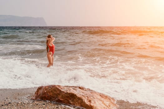 Woman travel sea. Young Happy woman in a long red dress posing on a beach near the sea on background of volcanic rocks, like in Iceland, sharing travel adventure journey