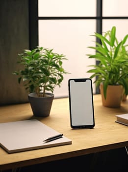 Smartphone on desk with blank screen, surrounded by plants and notebook.
