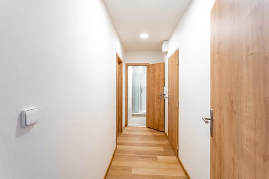 Well-lit, wooden-floored hallway in a contemporary home, showcasing multiple doors and clean design