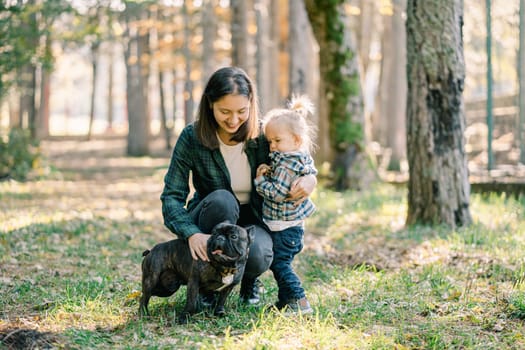 Mom hugs a little girl with one hand, squatting stroking the dog with the second. High quality photo