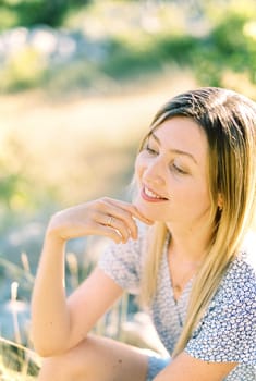 Smiling woman sitting on the grass touching her chin with her fingers. High quality photo