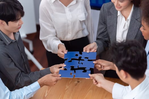 Corporate officer worker collaborate in office, connecting puzzle pieces with report paper on table as partnership and teamwork. Unity and synergy in business concept by merging jigsaw puzzle. Concord