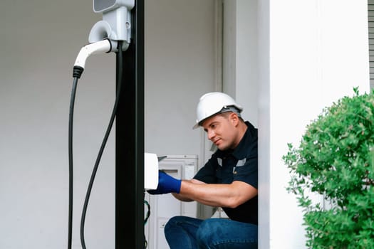 Qualified technician install home EV charging station, providing maintenance service for electric vehicle's battery charging platform at home. EV car technology for residential utilization. Synchronos