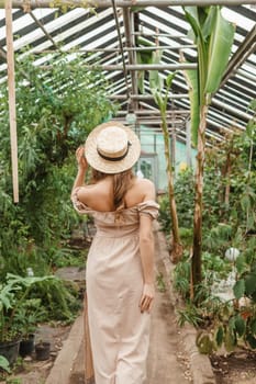 A beautiful young woman takes care of plants in a greenhouse. The view from the back. Concept of gardening and an eco-friendly lifestyle.