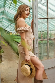 A beautiful young woman takes care of plants in a greenhouse. The concept of gardening and an eco-friendly lifestyle.