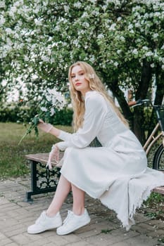 A blonde girl with long hair on a walk in a spring park. Springtime and blooming apple trees