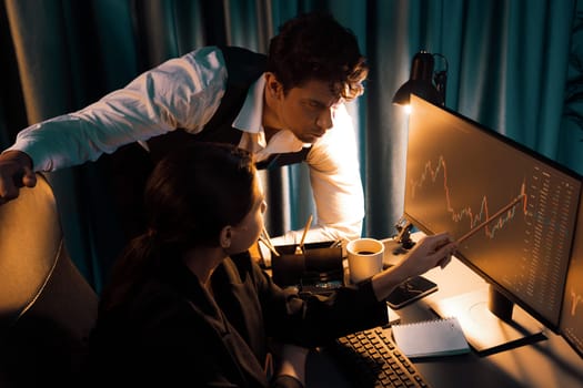 Two business traders discussing on dynamic stock exchange currency rate risk investment, pointing profit or loss value forecast on pc screens side view at night neon lighting office room. Postulate.