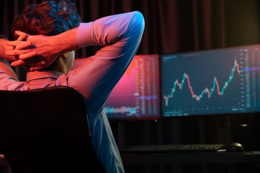Young investor stock trader leaning body back looking at investing dynamic screen of current market graph online in real time at neon light modern office, Concept of investment exchange rate. Gusher.