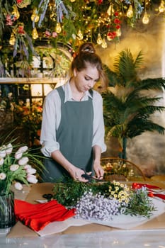 A woman in her florist shop collects bouquets of flowers. The concept of a small business. Bouquets of tulips for the holiday on March 8